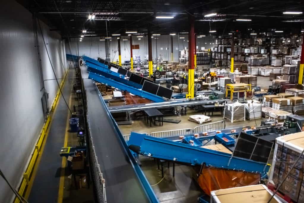 Conveyor Belt Tracking: Why Belts Wander and How Technicians Correct It 1 Long blue belt conveyors running overhead through a busy packing floor, the kind of takeaway lines where conveyor belt tracking needs regular checks